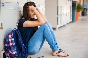 Girl sitting with her hands on her knees in front of lockers