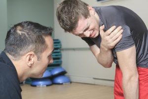 Man next to personal trainer holding shoulder in pain due to gym injury