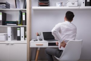 A man sat at a desk holding his lower back in pain.