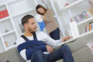 Man with a broken arm using his laptop to calculate compensation amounts for his personal injury claim