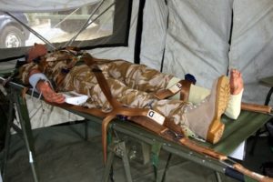 An armed forces soldier with a leg injury laying on a stretcher