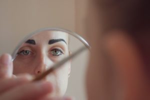 A woman looking at a mirror and applying makeup to her face