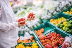 Some holding two red peppers in a supermarket.