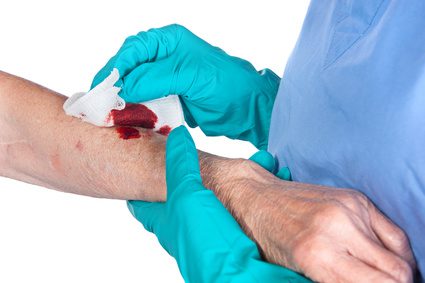 A medical professional cleaning up a cut on someone's arm with a white tissue.