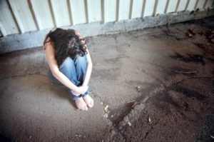 Woman sitting with her head on her knees on dirt