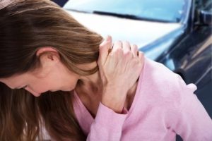 Woman holds her neck and injured shoulder. 