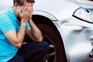 Man examines damaged car after a road traffic accident with his head in his hands.