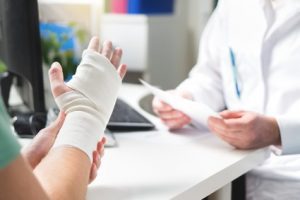 An injured person with bandages around their hand and wrist visits a doctor providing treatment