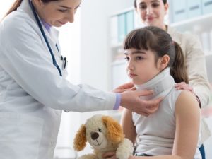 A child wearing a neck-brace being examined by a doctor