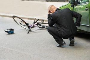 Man kneeing over a knocked over bicycle with the helmet on the ground