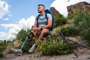 Man with prosthetic right leg sits on a rock while on a hike after a leg amputation