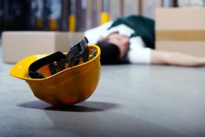 A worker laying on the floor in the background following an accident. In the foreground is his discarded hard hat.