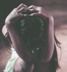 A young girl holding her head while kneeling in distress