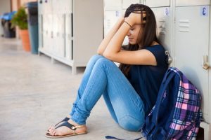 A girl sitting down in front of her locker holding her head up while crying
