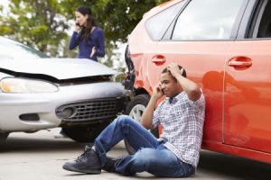 A man without insurance on the phone on the floor after a car accident