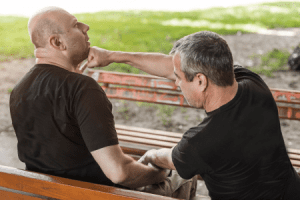 A man inflicting actual bodily harm on another man while sitting on a bench