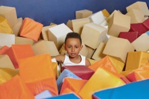 A child sat in an indoor soft play area with foam blocks.