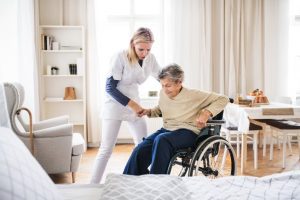 Worker moving an older client from a wheelchair onto a bed