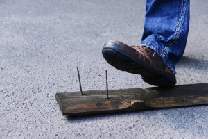 Man about to step on nail sticking out of a plank of wood