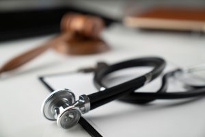 A stethoscope in the foreground, with a judge's gavel in the background and slightly blurred.