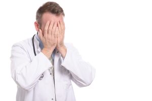 a doctor in a white coat with stethoscope around neck and head in his hand. 