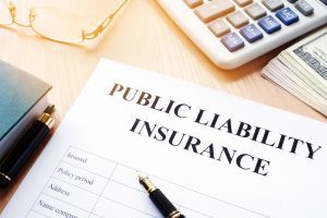 A public liability insurance form on a desk with a fountain pen, a calculator, a stack of banknotes and a pair of glasses.