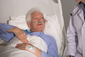 A cancer patient lies in a hospital bed and looks up at a doctor who is standing beside them.