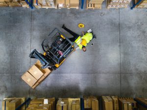 A warehouse worker injured due to an employer's negligence, lying on the floor next to a forklift 