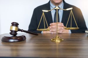 A solicitor sits behind a gold set of scales and a dark wooden gavel.