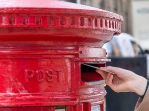 A letter being put into a red letterbox. Post being sent to the wrong address could be an example of a data protection breach.