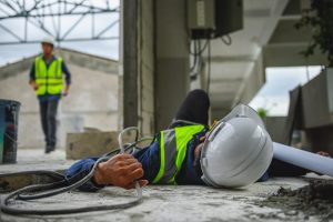 A construction worker lying on the floor after tripping over a trailing leads hazard.