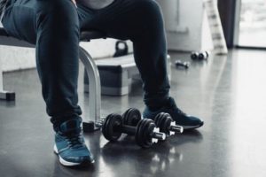 Man inside a gym sitting near dumbbells on the floor