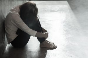 A woman sits huddled on the floor. 