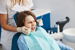 A child sits in a chair and undergoes a dental procedure causing an unusual or uncomfortable feeling
