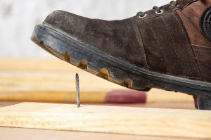A foot in a work boot gets a nail puncture wound from standing on a nail