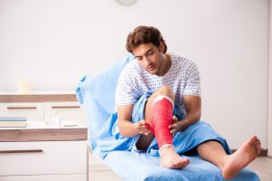A person sits on a hospital bed with their lower leg bandaged. 