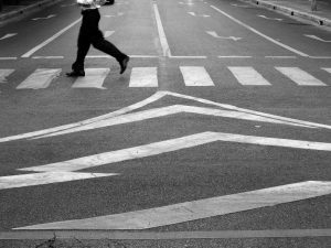 A black and white image of a person walking on a zebra crossing.