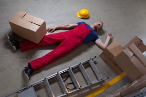 A warehouse worker lays on the floor unconscious following a ladder fall accident.