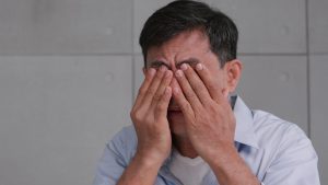 A man rubs his eyes due to the pain