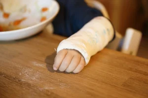 A closeup image of a young boy's arm which is wrapped in a cast with writing on it.