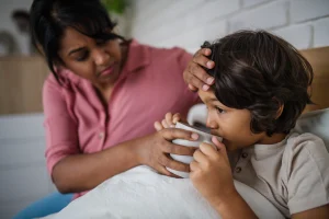 A mother helping her poorly child drink from a mug after suffering from negligent medical treatment.