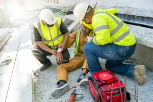 A builder suffers an injury at a construction site and is seen to by two colleagues in high-vis vests.