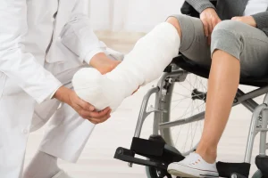 Doctor examining a patient with a leg injury in a cast while the patient sits in a wheelchair.